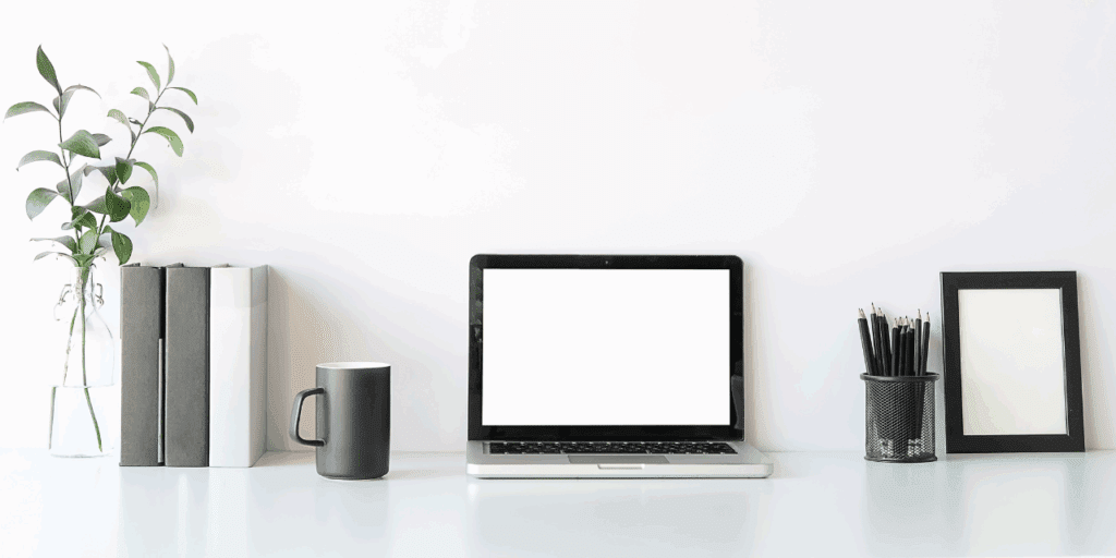An organized workspace with a coffee mug, laptop, jar of black pencils, neatly placed binders, and a eucalyptus branch.