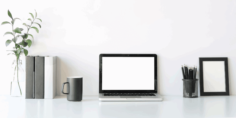 An organized workspace with a coffee mug, laptop, jar of black pencils, neatly placed binders, and a eucalyptus branch.