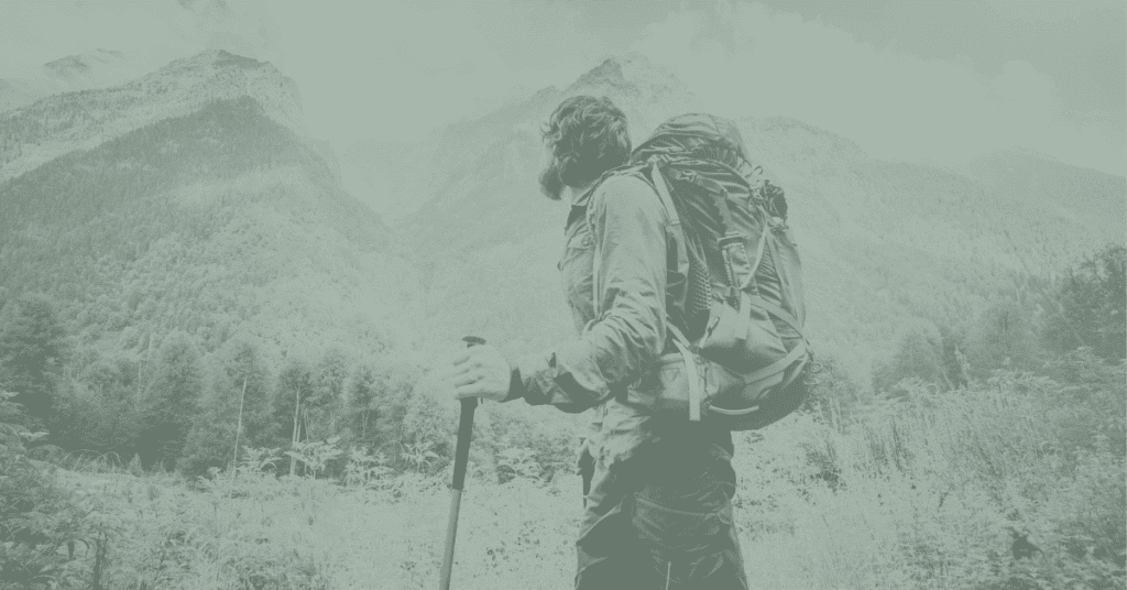 Image shows a man hiking along a trail in front of mountains
