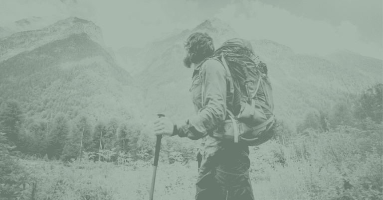 Image shows a man hiking along a trail in front of mountains